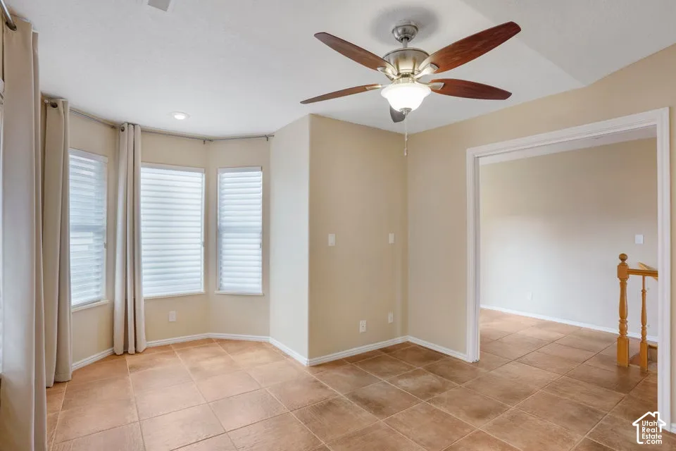 Room featuring neutral-tone ceramic tile flooring, bay windows with horizontal blinds, a vaulted ceiling, and a central ceiling fan with integrated lighting