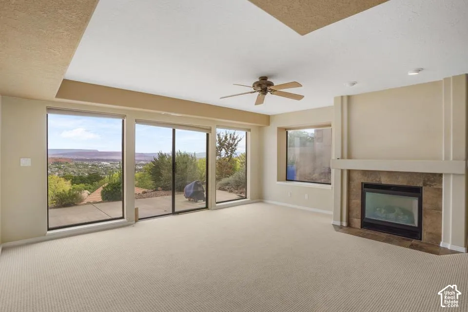 Living space featuring a coffered ceiling, stone-surround fireplace with a mantel, floor-to-ceiling windows, sliding glass door, and ceiling fan