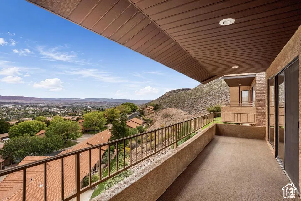 Covered balcony with textured flooring, metal railing, and recessed ceiling lighting, featuring an expansive mountain and valley horizon
