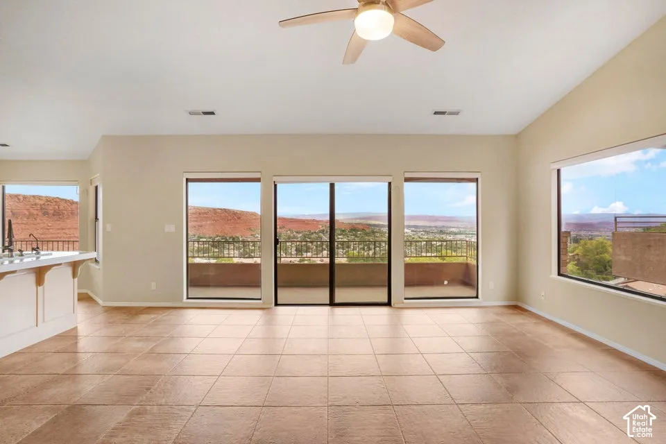 Open-concept room featuring large windows, sliding glass doors, neutral tile flooring, vaulted ceilings, and an integrated ceiling fan