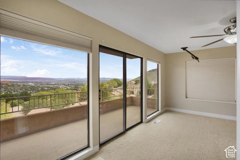 Floor-to-ceiling windows, sliding glass door with access to a balcony, carpeting, ceiling fan, and mountain scenery