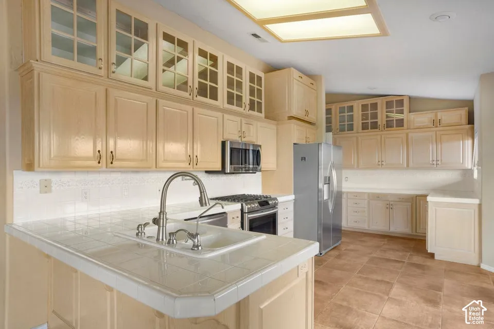 Kitchen featuring light-tone cabinetry with glass-panel upper doors, tile countertops, recessed ceiling lighting, and large-format tile flooring