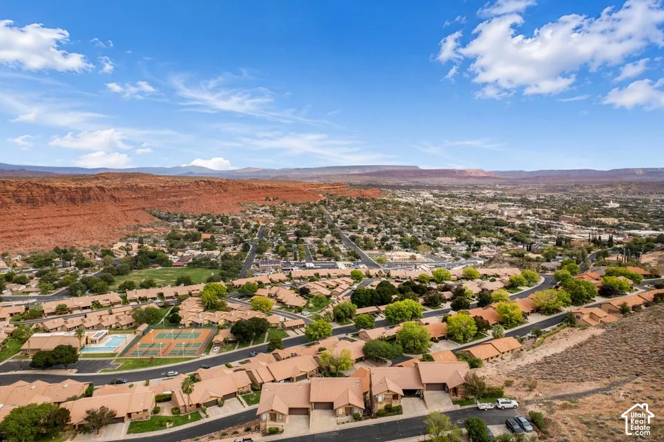 Aerial perspective of a residential community featuring terracotta-tiled roofs, red rock mountain backdrops, and proximity to tennis courts and a swimming pool