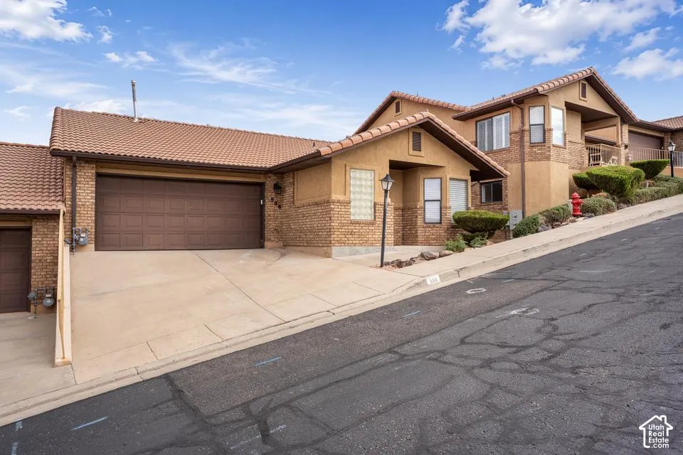 Stucco and brick facade with a clay tile roof, multi-level architectural profile, concrete driveway, and attached garage