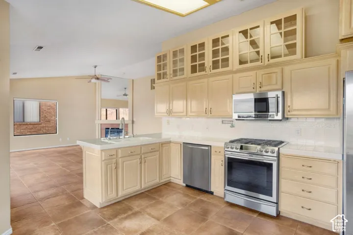 Kitchen featuring light-toned cabinetry with glass-front uppers, tile countertops, stainless steel appliances, and large-format tile flooring