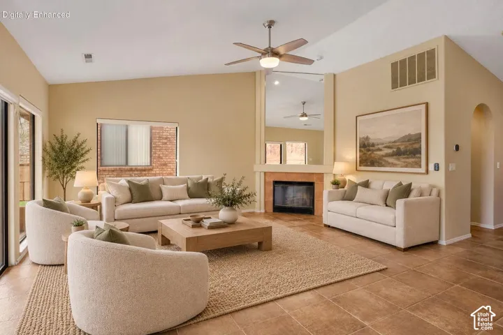 Vaulted ceiling with a central brushed metal ceiling fan, fireplace with a tiled hearth and a floor-to-ceiling mirror, and ceramic tile flooring