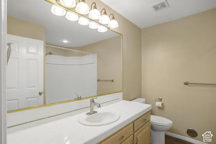 Bathroom vanity featuring tile countertops, integrated oval basin, light wood-finish cabinetry, full-width wall mirror, and six-light vanity fixture