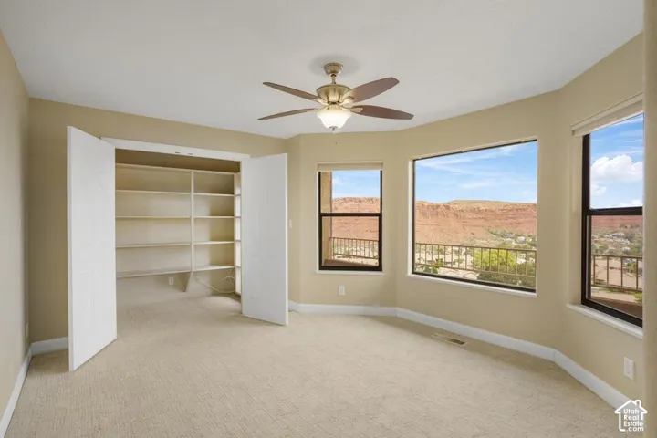 Bay windows with mountain landscape scenery, built-in shelving, carpeted flooring, and a ceiling fan with integrated lighting