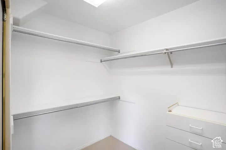 Storage space featuring tiered shelving, integrated clothing rods, and a built-in cabinetry unit with three drawers