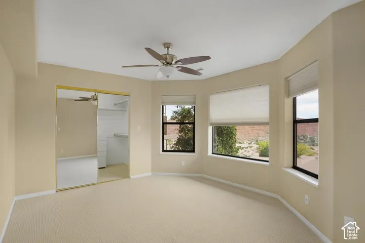 Room featuring carpeted flooring, a ceiling fan with integrated lighting, a bay window configuration, and mirrored sliding closet doors