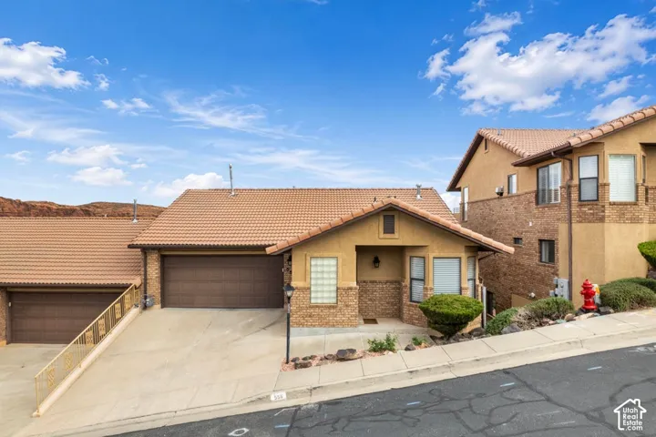 Multi-level residence featuring a stucco and stone veneer exterior, clay tile roofing, attached multi-car garages, and recessed entryway