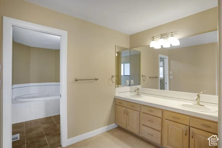 Double vanity with light-wood cabinetry, white tile countertops, dual under-mount sinks, and wall-to-wall mirror with four-light fixture