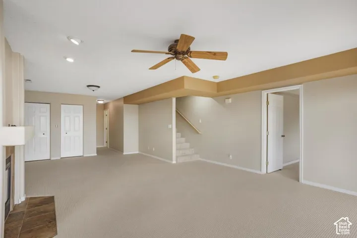 Neutral carpeted flooring, ceiling fan with light fixture, recessed lighting, and a fireplace with stone-finish hearth