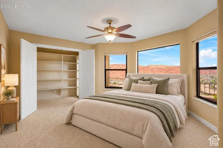 Room featuring expansive windows, red rock mountain scenery, built-in closet shelving, neutral carpeting, and a ceiling fan with integrated lighting