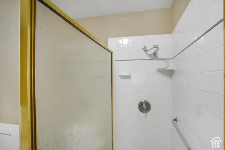 Shower enclosure featuring white wall tiling, a gold-trimmed frame, a metallic showerhead, built-in soap dish, and a metallic wall-mounted grab bar