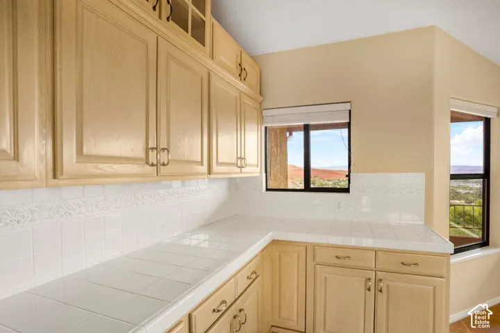 Light-finish cabinetry featuring upper glass-panel displays, white tile countertops, and a coordinated white tile backsplash with decorative inset detailing