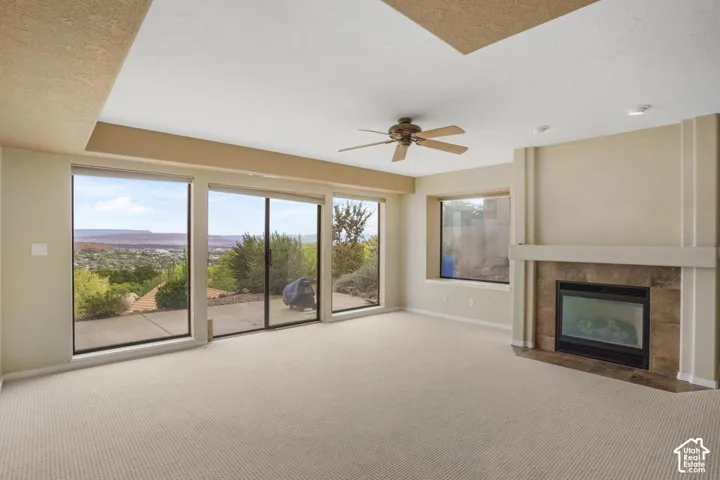 Living space featuring a coffered ceiling, stone-surround fireplace with a mantel, floor-to-ceiling windows, sliding glass door, and ceiling fan
