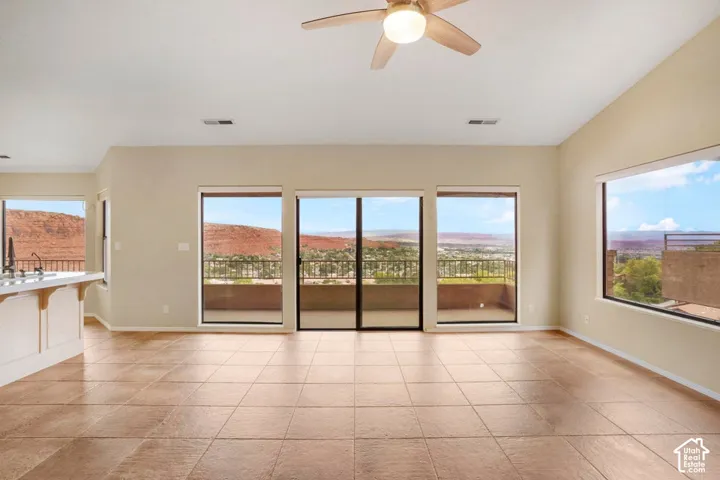Open-concept room featuring large windows, sliding glass doors, neutral tile flooring, vaulted ceilings, and an integrated ceiling fan
