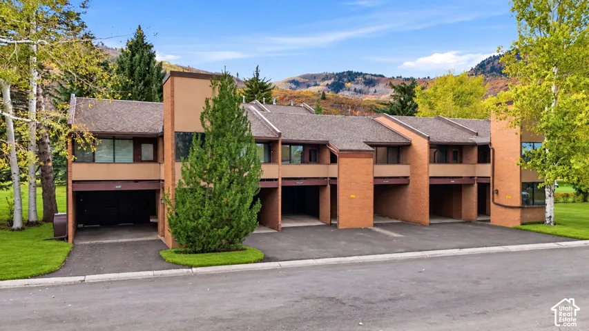 Multi-unit structure featuring brick masonry exterior, asphalt shingle roofing, and covered ground-level parking bays set against a mountain landscape