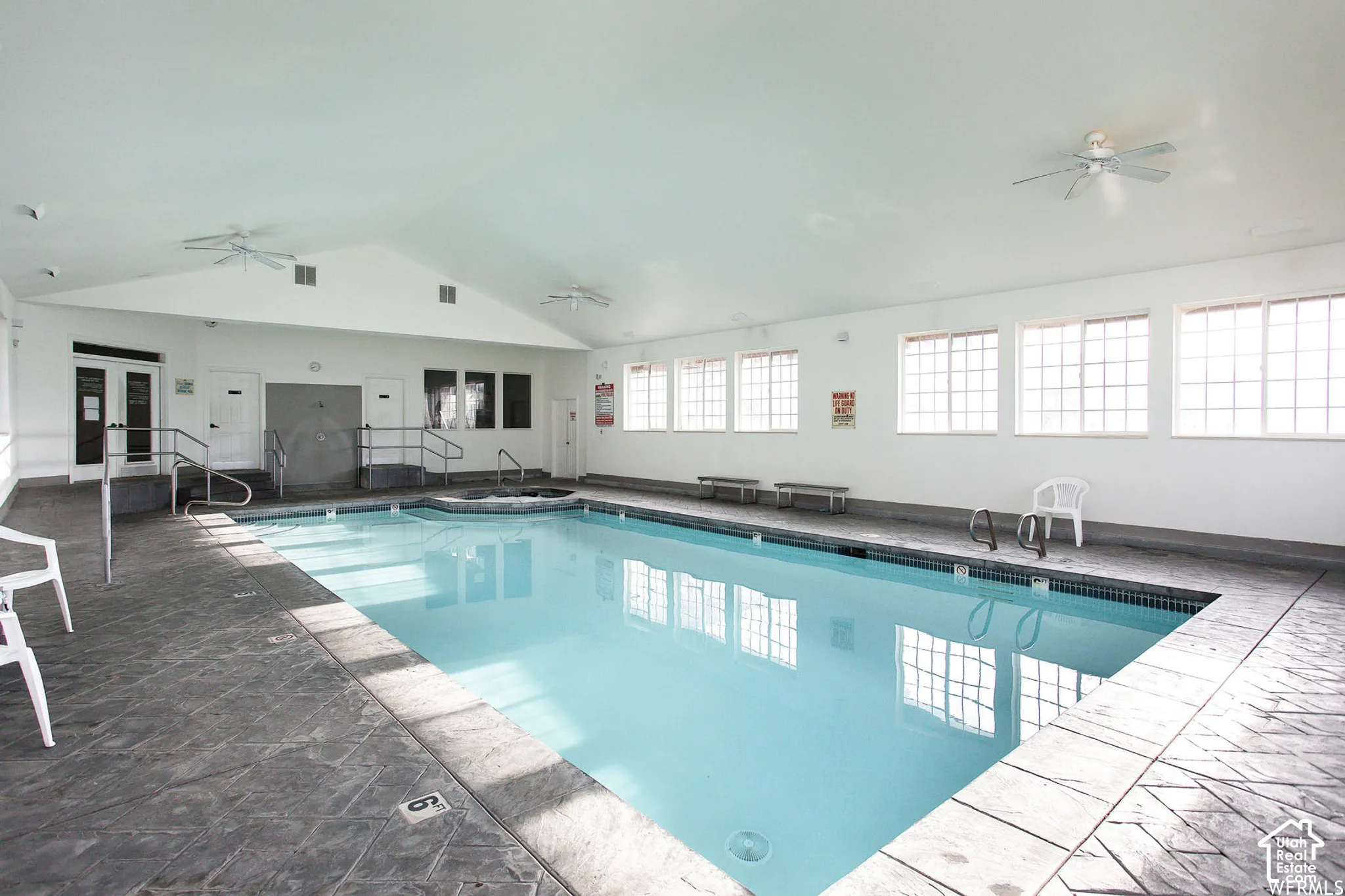 Indoor swimming pool featuring an expansive swimming area, a built-in spa, textured concrete flooring, vaulted ceilings, and multi-pane windows