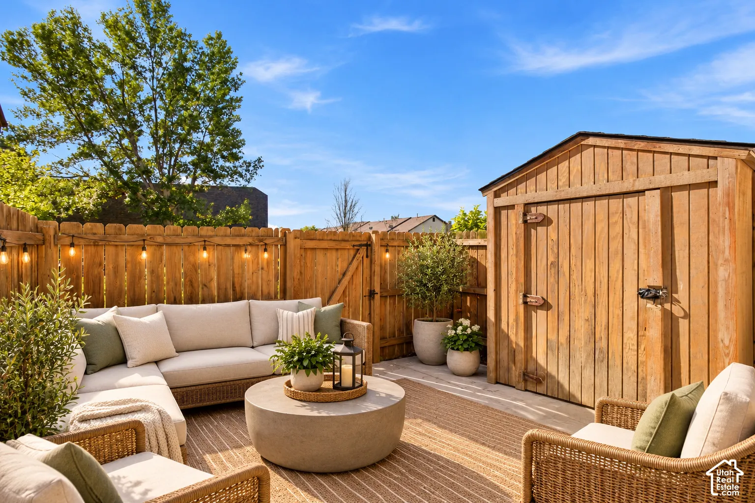Concrete patio space featuring a wood-panel fence, integrated string lighting, and an attached vertical-siding storage structure