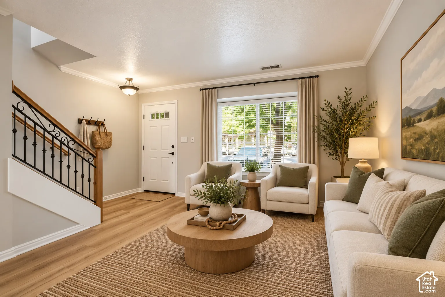 Wood-finish flooring, staircase with a wood handrail and decorative metal balusters, crown molding, and a paneled entry door