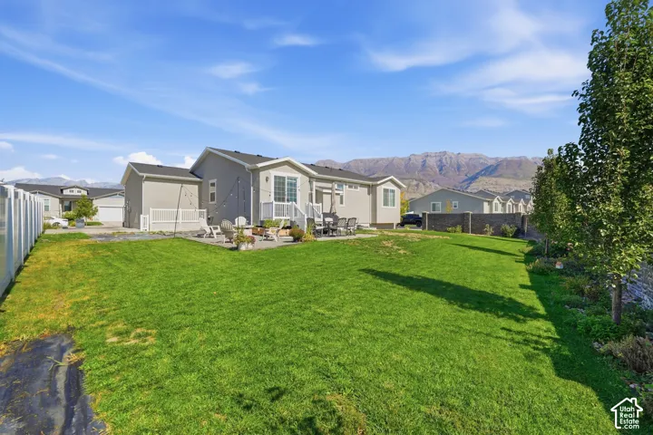 Expansive backyard featuring a manicured lawn, stone patio, perimeter privacy fencing, and mountain backdrop