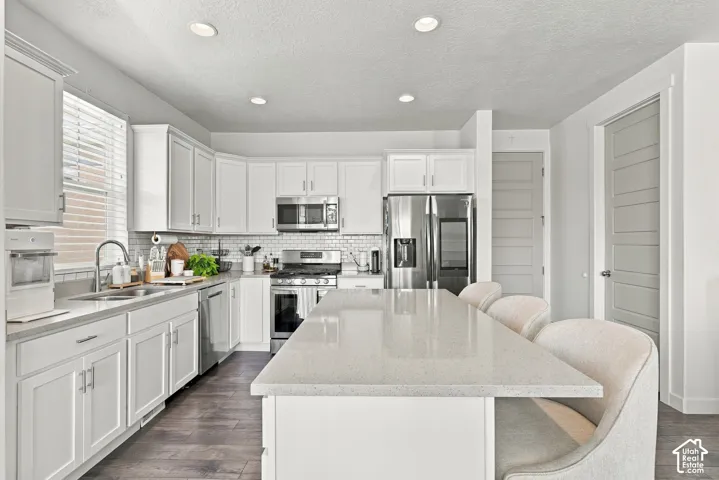 Kitchen featuring white shaker-style cabinetry, quartz countertops, subway tile backsplash, stainless steel appliances, and wood-finish flooring