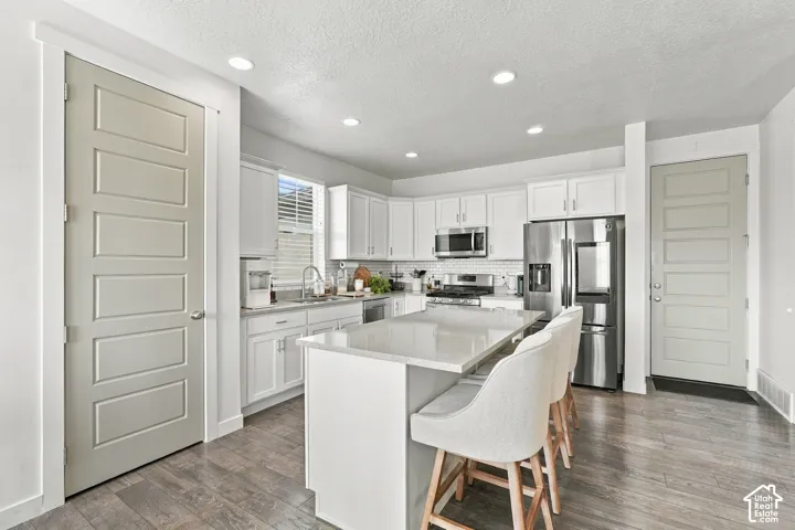 Kitchen featuring white cabinetry, an island with stone-finish countertop, stainless steel appliances, recessed ceiling lighting, and wood-finish flooring