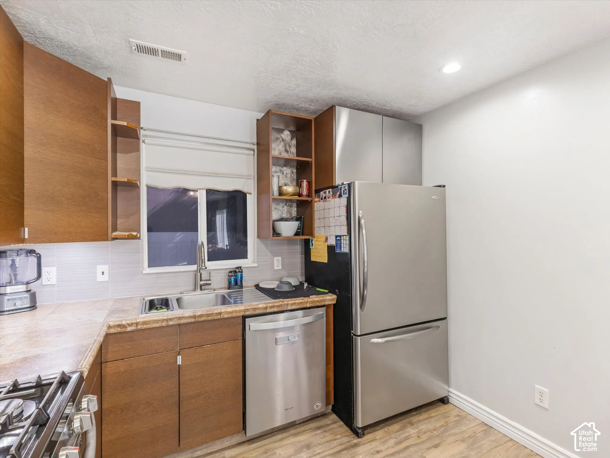 Kitchen area featuring wood-finish cabinetry, stainless steel appliances, tile backsplash, wood-finish flooring, and a single-basin sink
