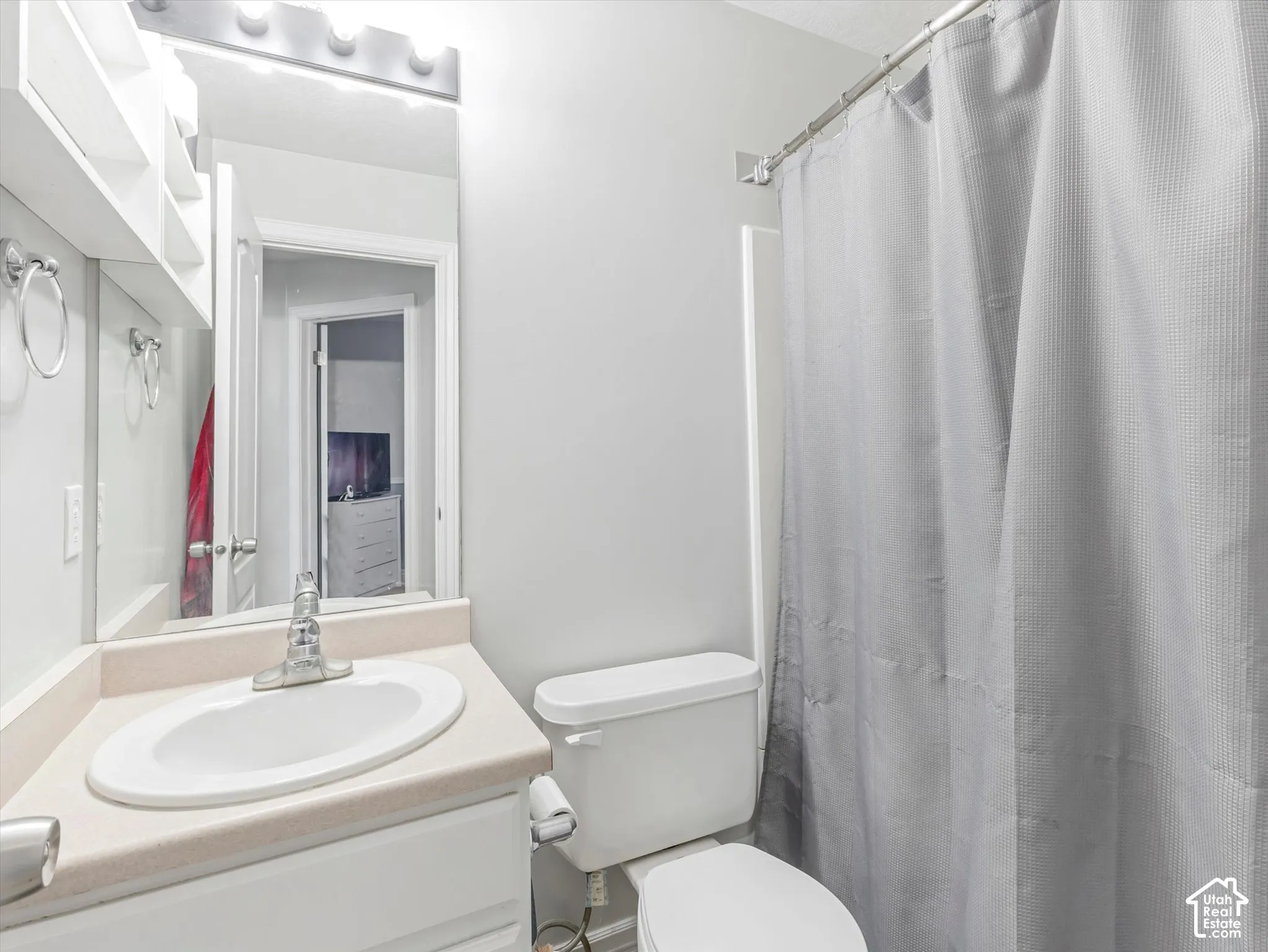 Bathroom featuring a white vanity with an integrated oval sink, countertop, wall-mounted light fixture, full-width mirror, and a shower-tub combination with a curtain rod