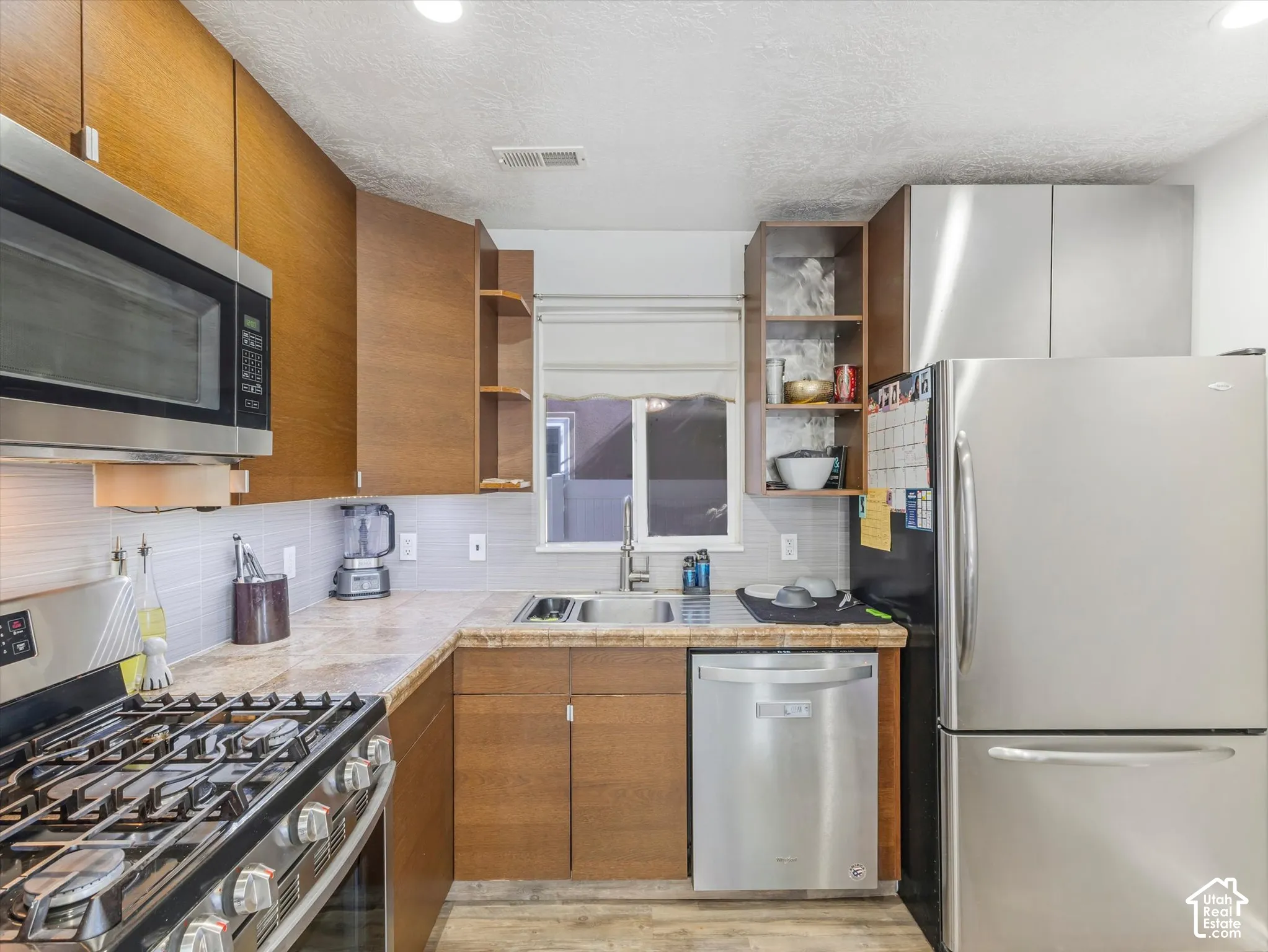 Kitchen featuring wood-finish cabinetry, stainless steel appliances, stone-finish countertops, recessed lighting, and open shelving