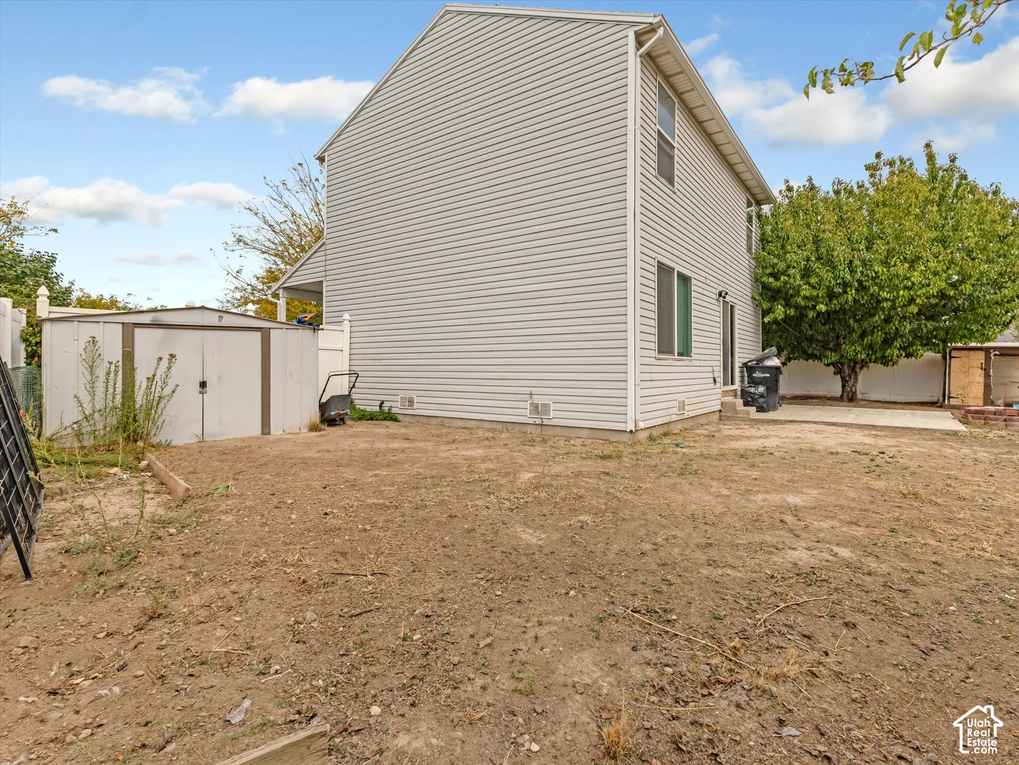 Two-story exterior featuring light-colored horizontal siding, a concrete rear patio, and a detached metal storage structure enclosed by perimeter fencing