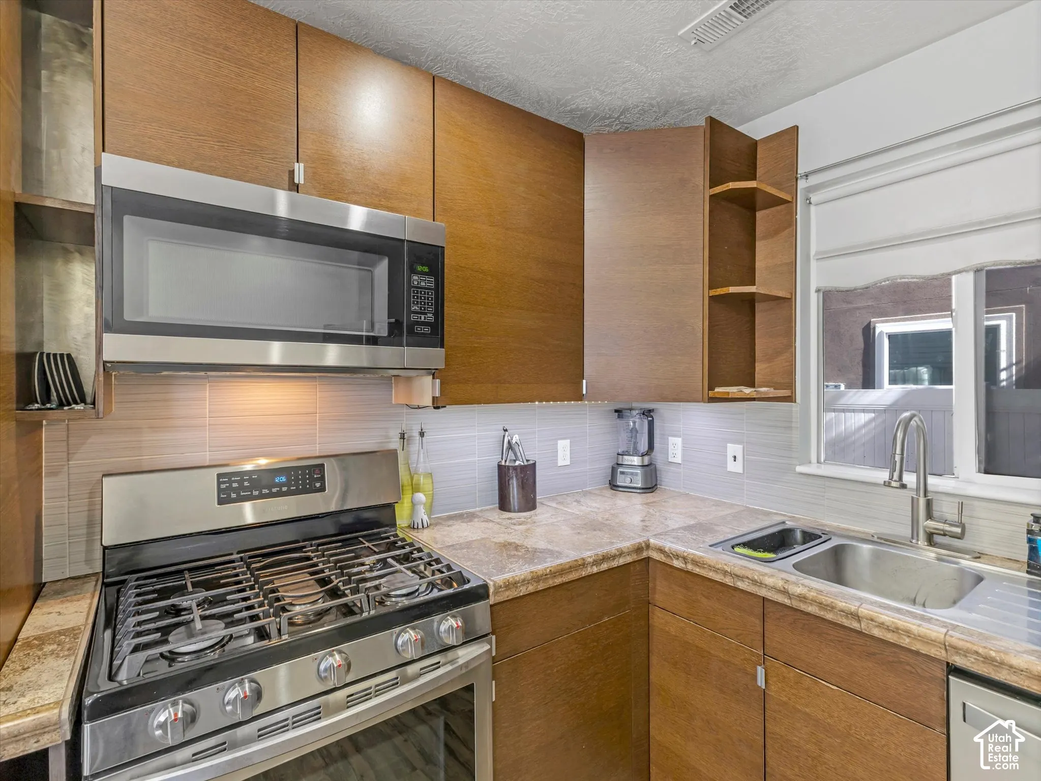 Kitchen featuring wood-finish cabinetry, stainless steel gas range, built-in microwave, stone-finish countertops, and an undermount stainless steel sink