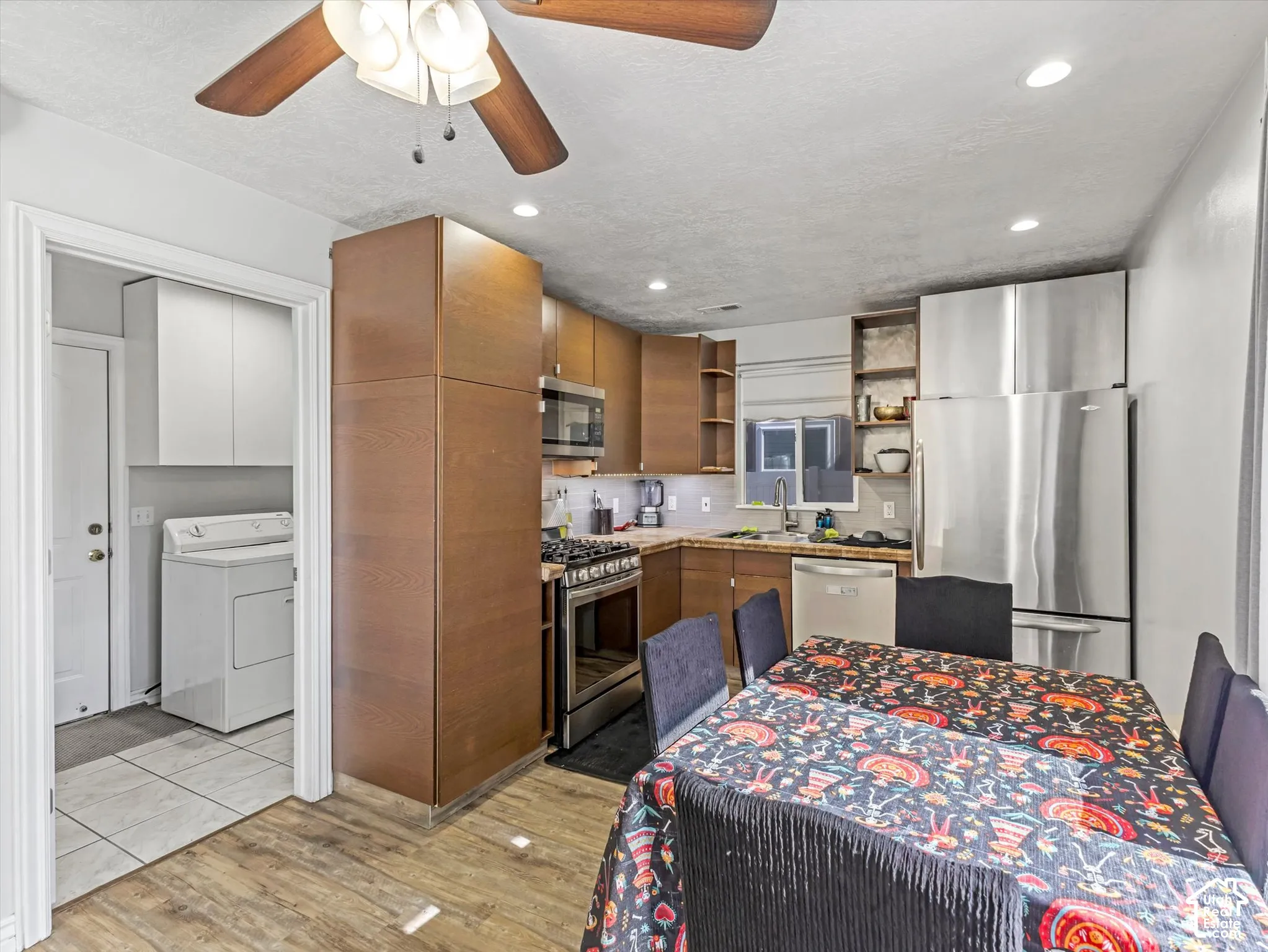 Kitchen featuring wood-finish cabinetry, stainless steel appliances, and wood-finish flooring, accompanied by a utility room with tile flooring