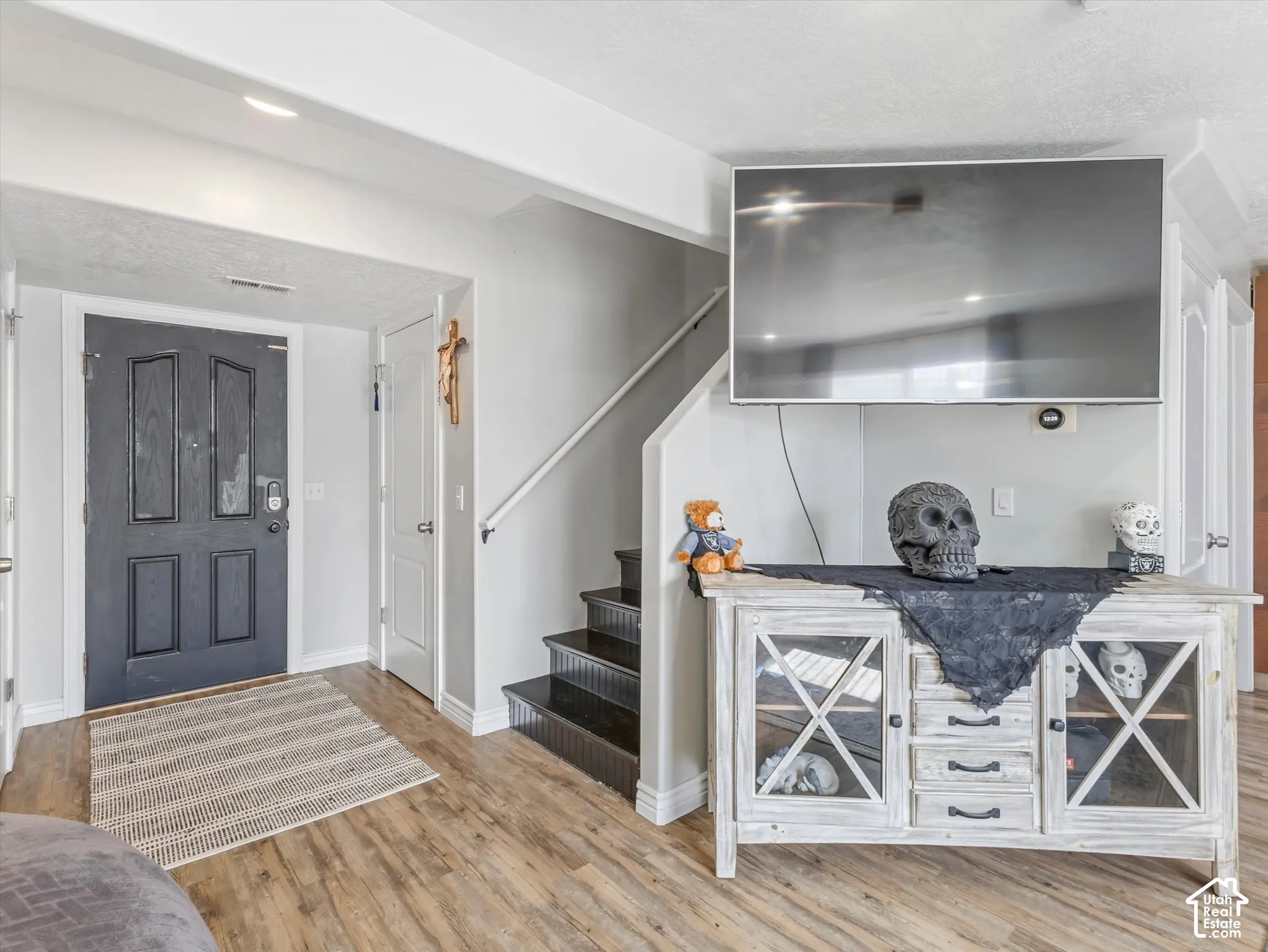 Entryway featuring wood-finish flooring, a dark-toned four-panel front door, and a staircase with dark treads and a white handrail