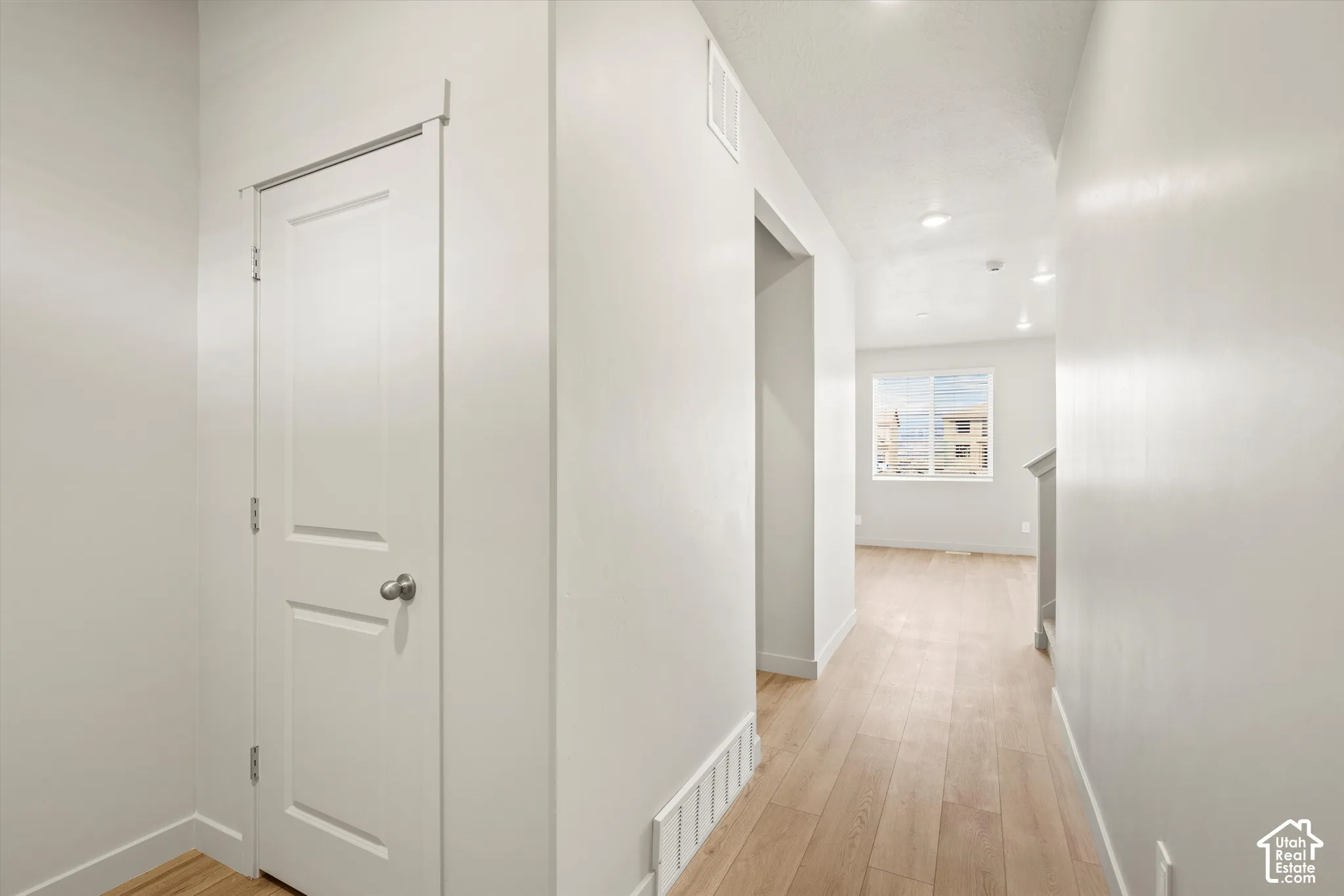 Interior hallway featuring light-toned wood-finish flooring, recessed ceiling lighting, and a single-panel interior door