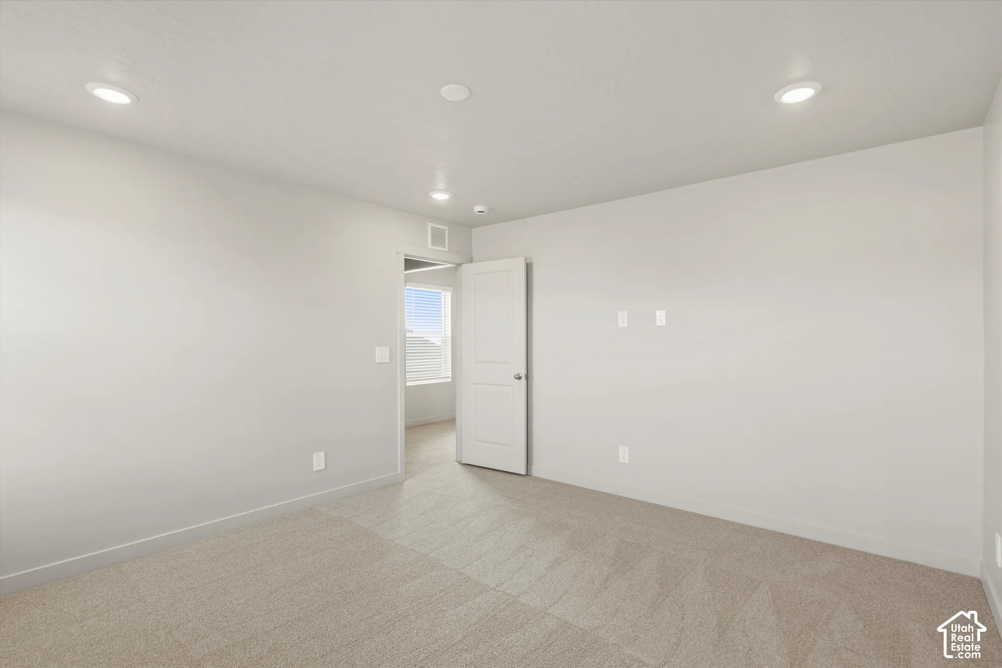 Neutral-toned interior space featuring recessed ceiling lighting, light-colored carpeting, and a solid-core interior door
