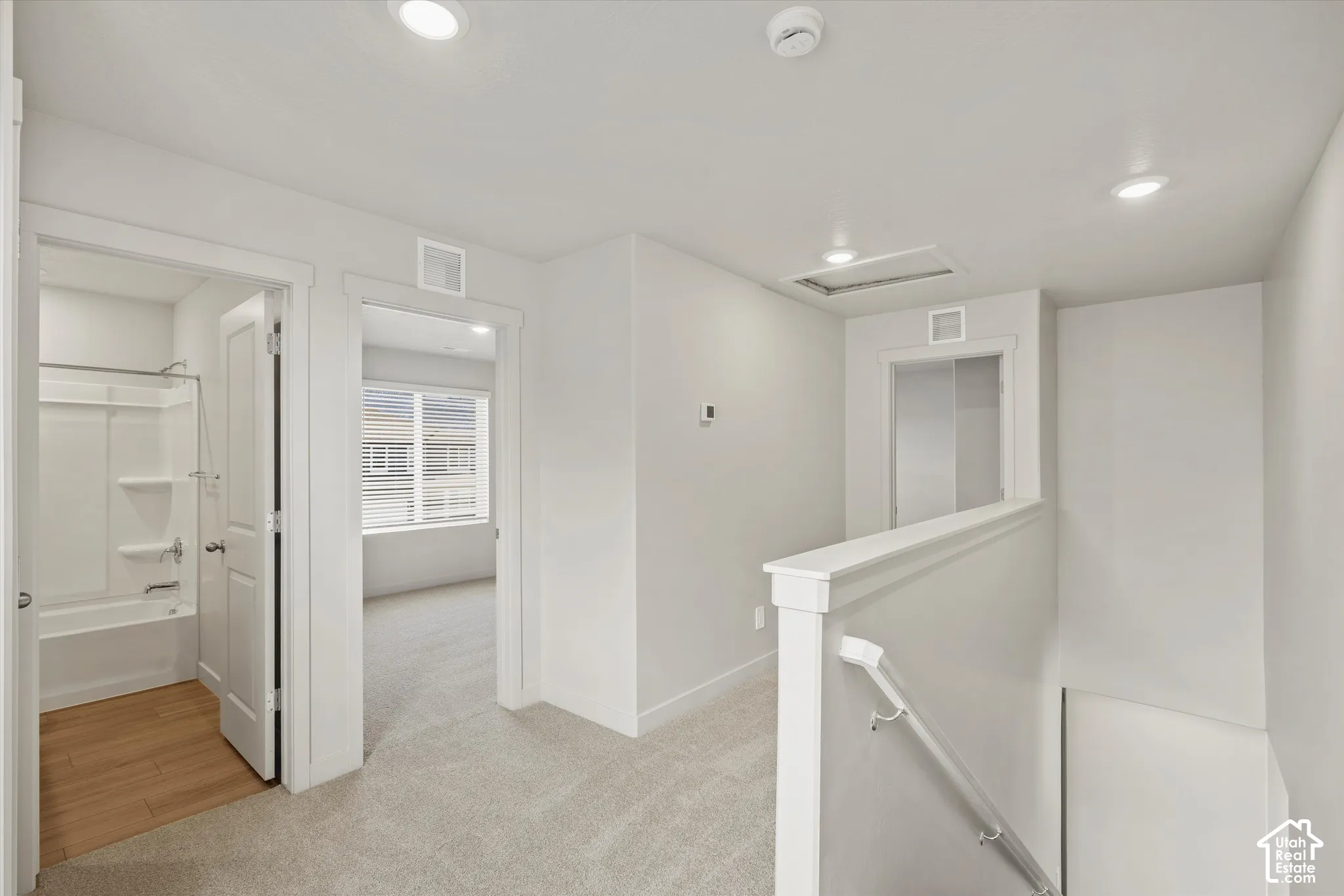 Neutral-toned carpeting, recessed ceiling lighting, stairway with white handrail, and bathroom featuring a tub-shower combination with wood-finish flooring