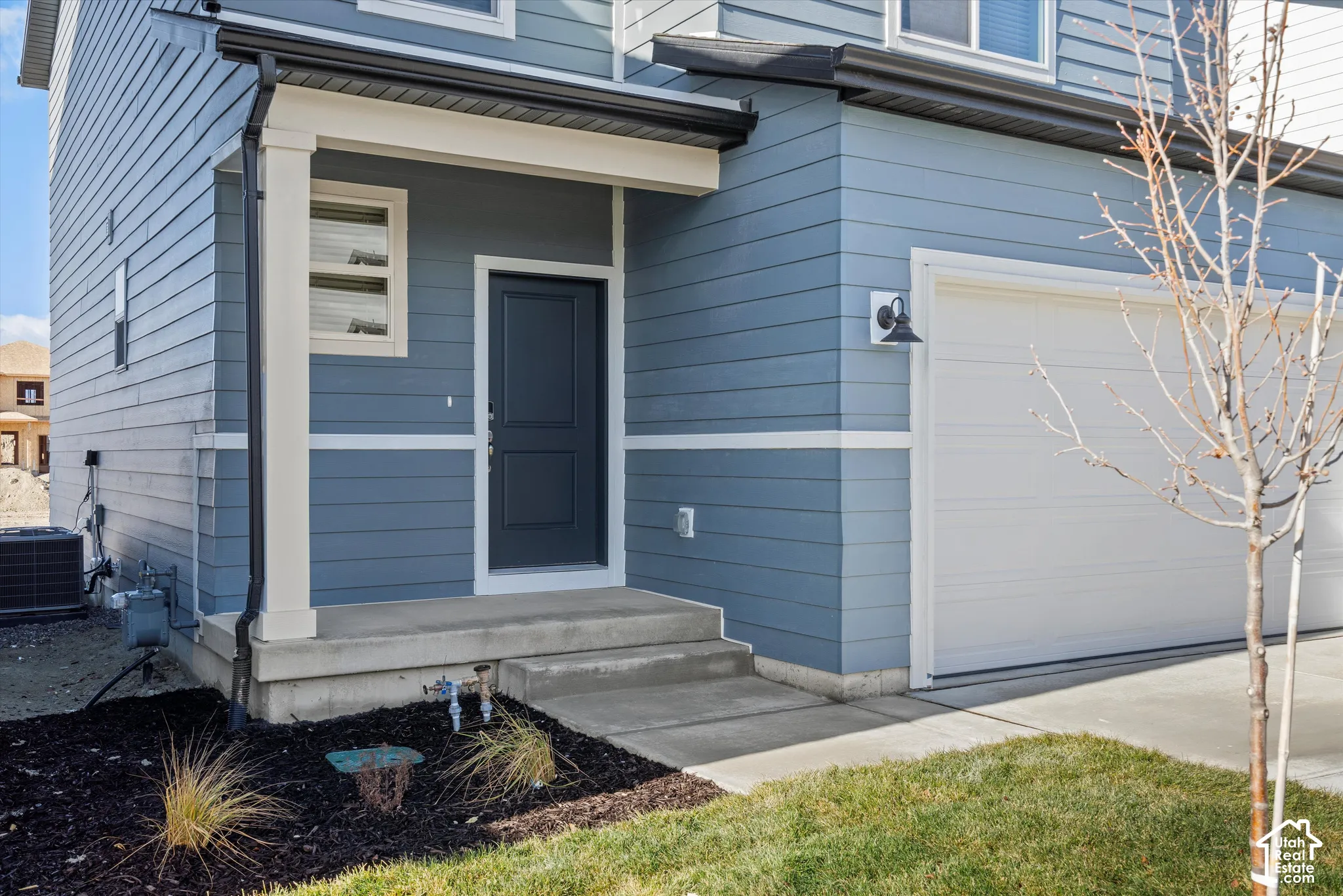 *DISCLAIMER* Elevation and exterior color may vary. Exterior featuring horizontal lap siding, a concrete porch, a paneled front door, a multi-section garage door, and metal exterior light fixtures
