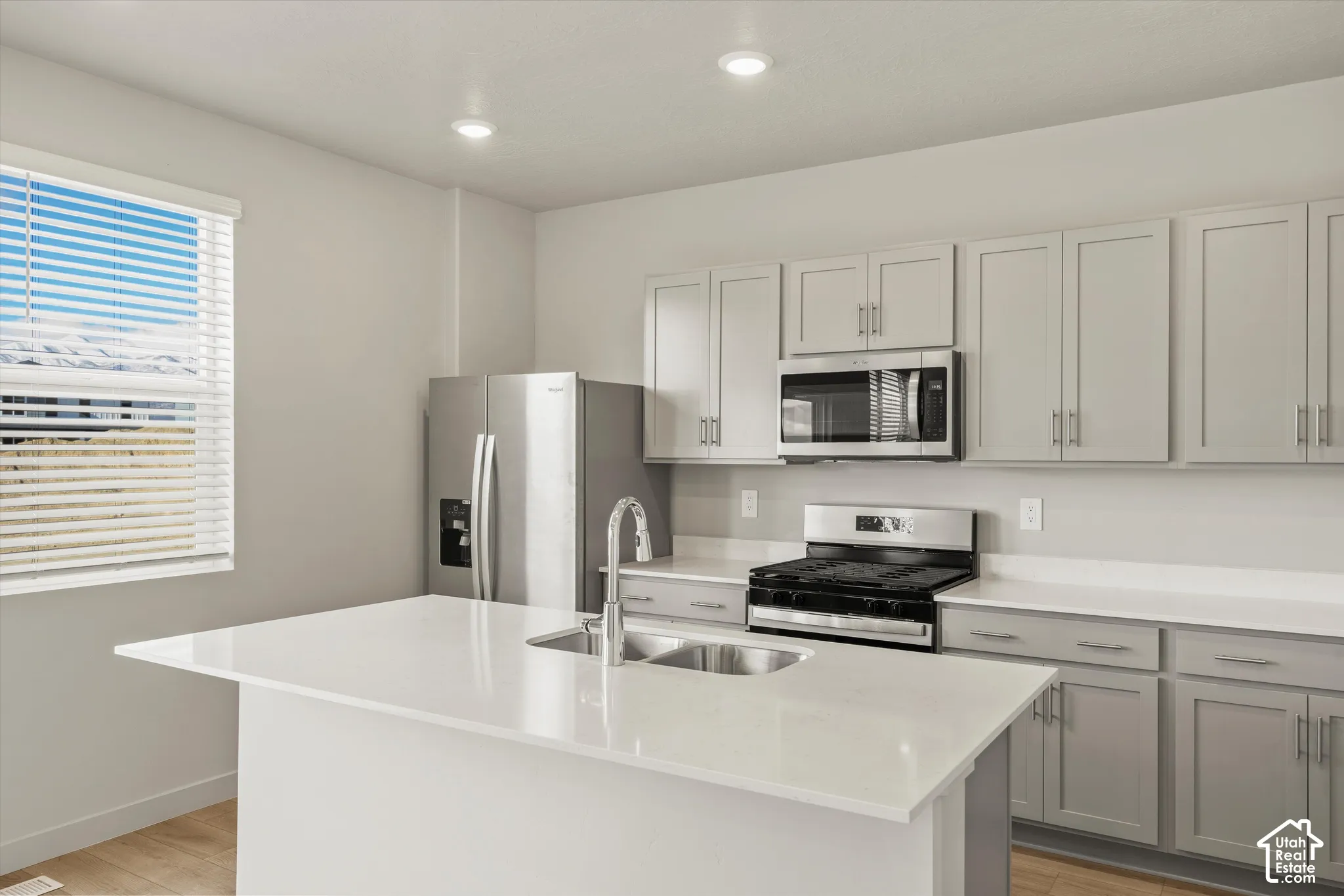 Kitchen featuring a central island with a quartz countertop, stainless steel appliances, neutral-toned cabinetry, recessed lighting, and wood-finish flooring