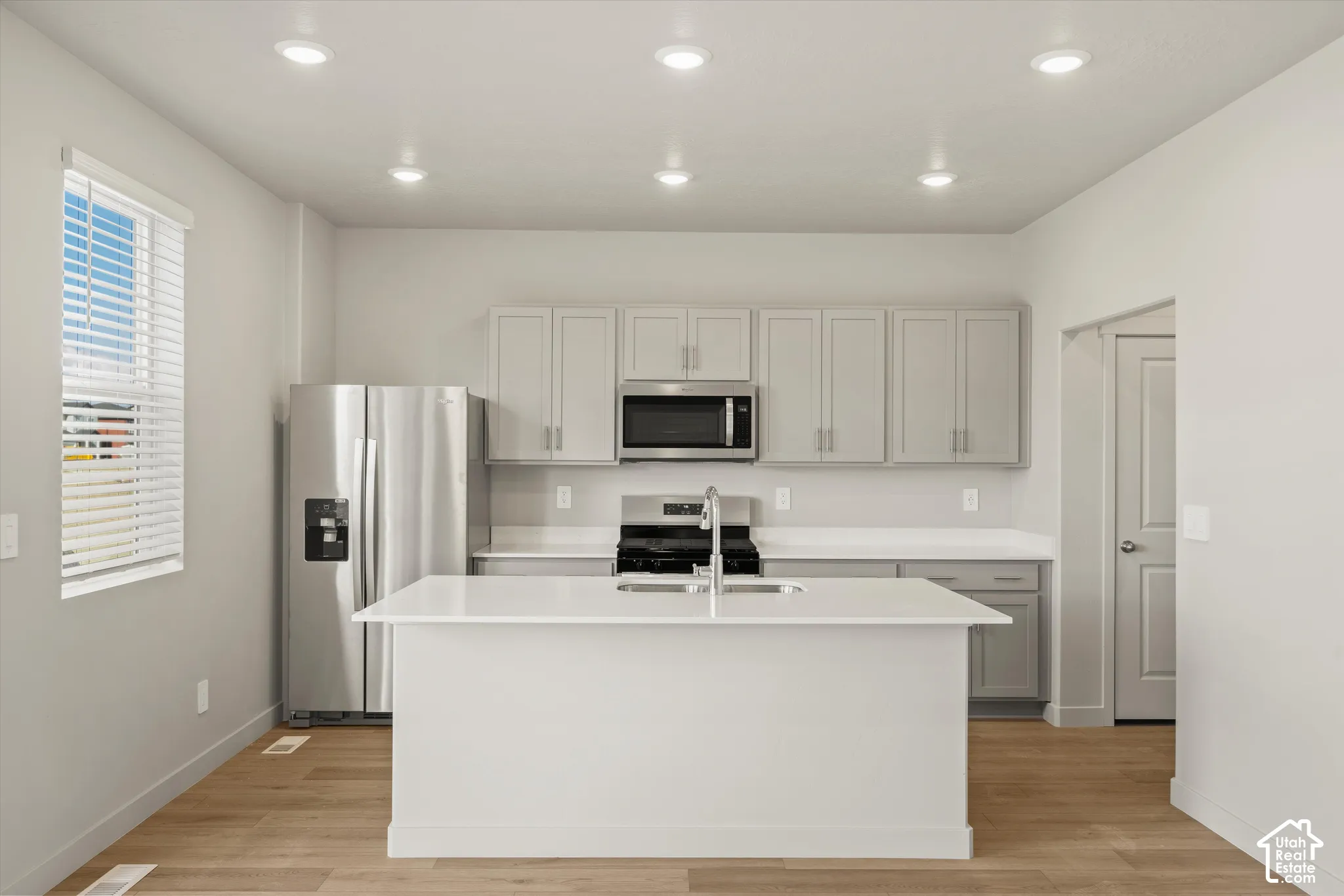 Kitchen featuring a central island with a solid surface countertop, wood-finish flooring, stainless steel appliances, recessed ceiling lighting, and grey shaker-style cabinetry