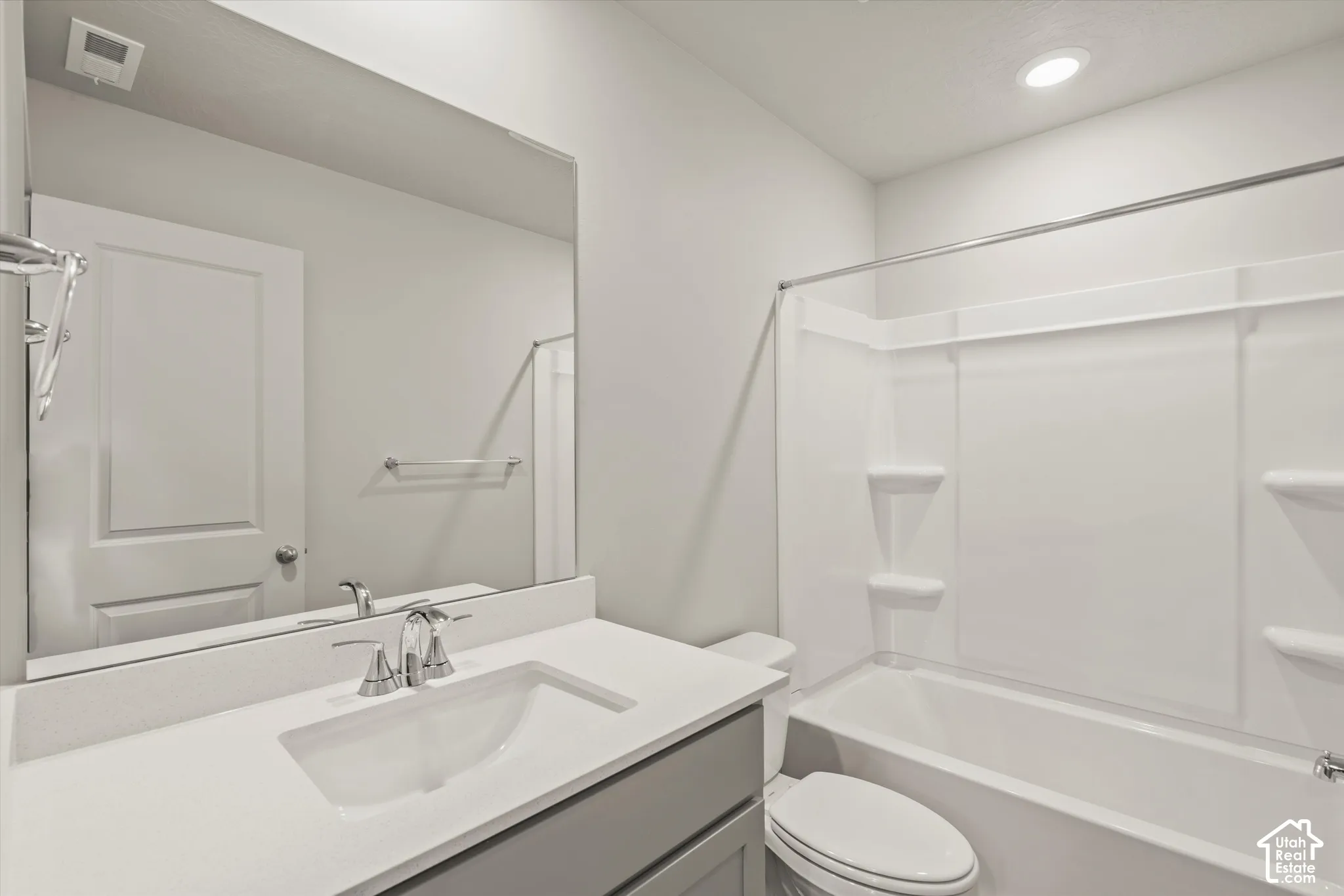 Bathroom featuring a vanity with a white solid-surface countertop, an undermount sink, a large wall-mounted mirror, and a combined tub and shower unit