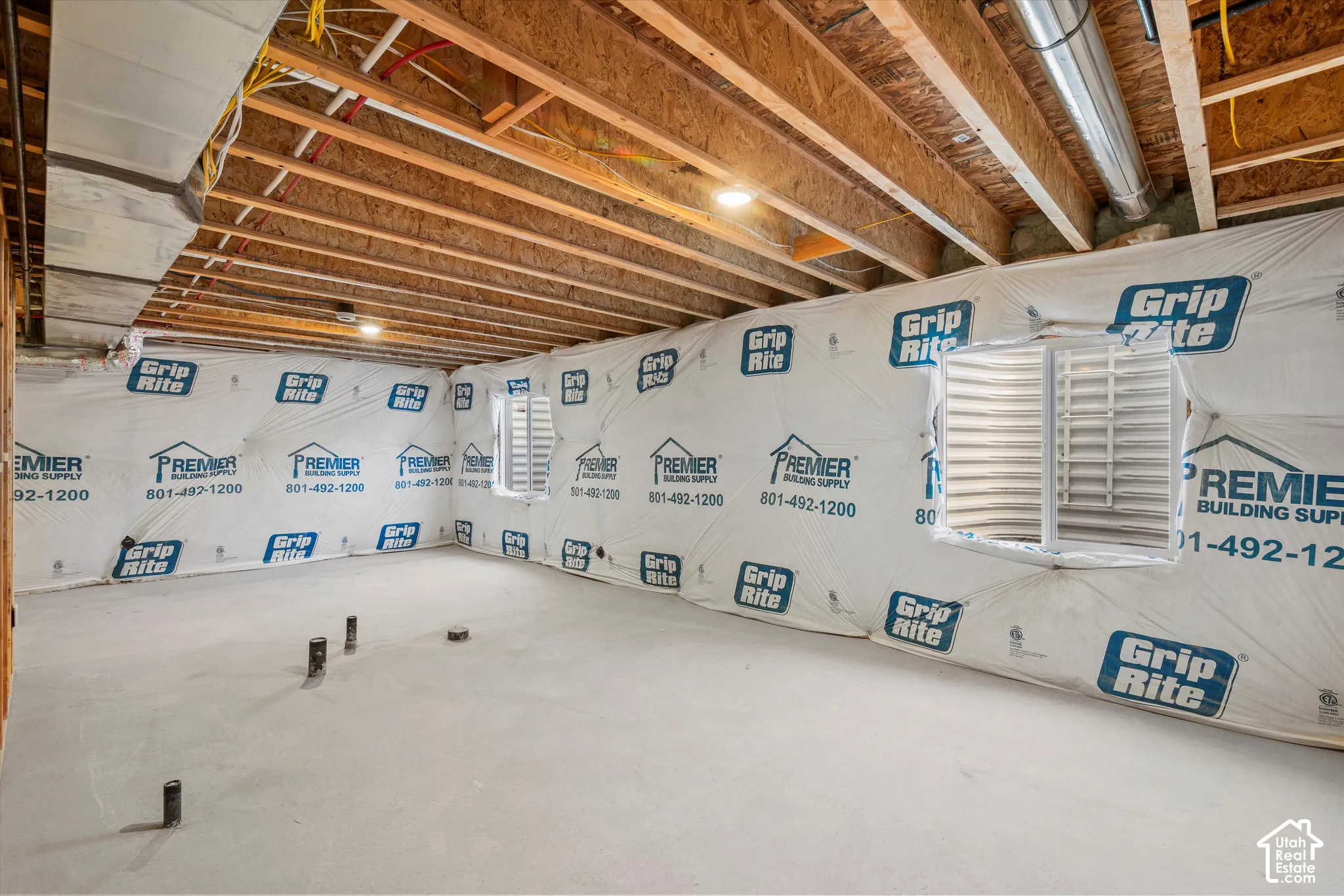 Unfinished space featuring exposed ceiling joists, concrete flooring, vapor barrier foundation wall coverings, and two window wells