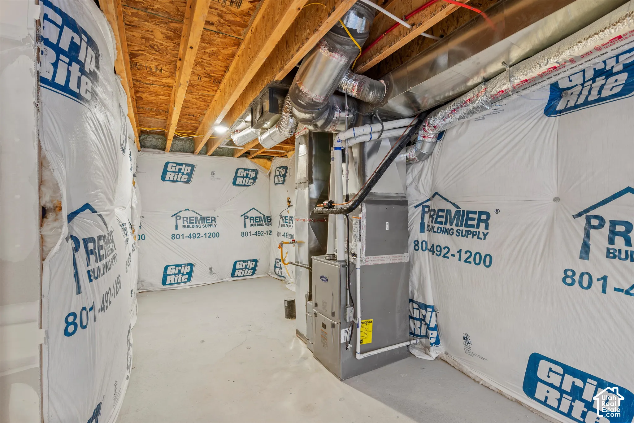 Utility area featuring a furnace, exposed wooden ceiling joists, concrete floor, and insulation-wrapped wall panels