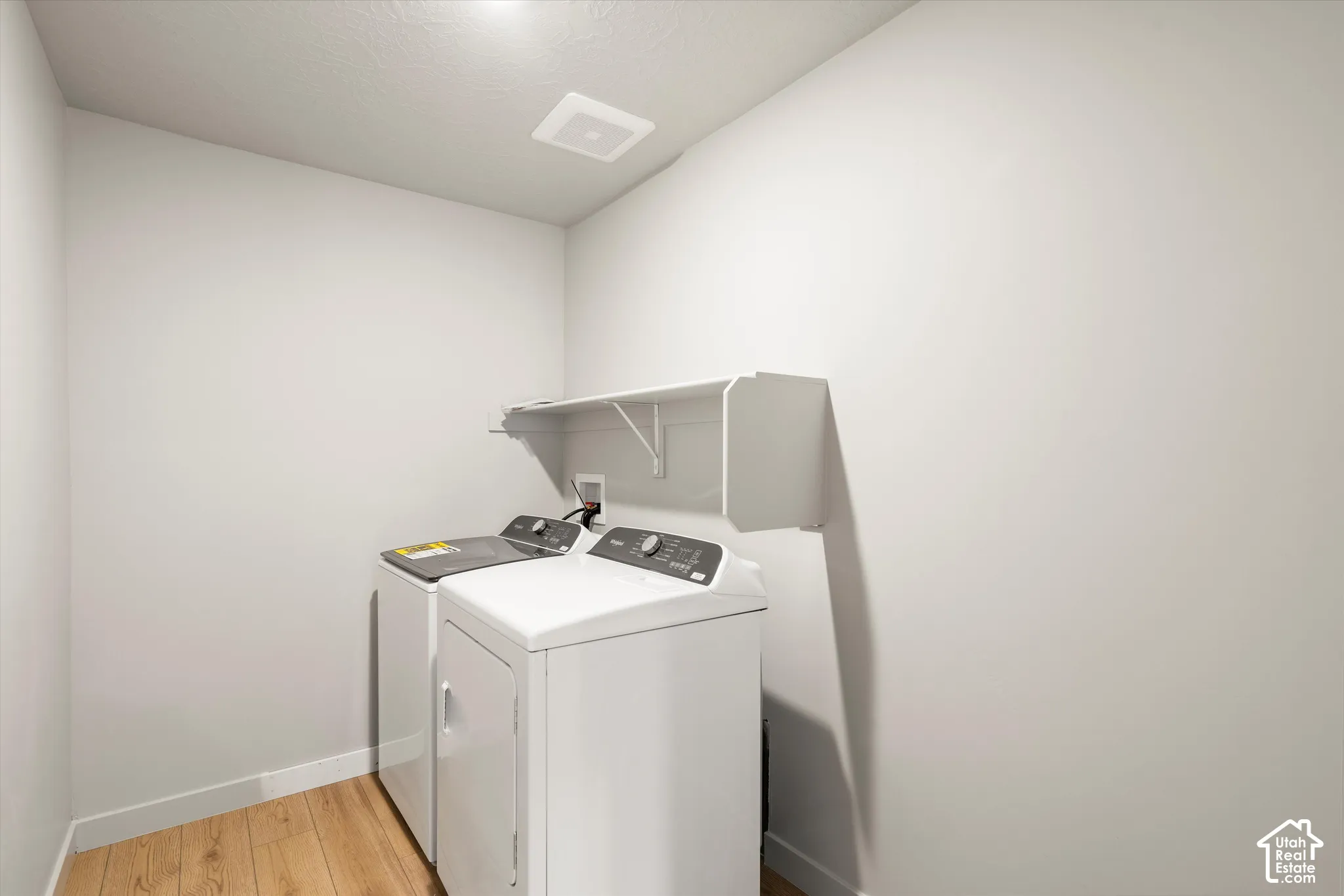 Dedicated laundry area featuring wood-finish flooring and wall-mounted storage shelving
