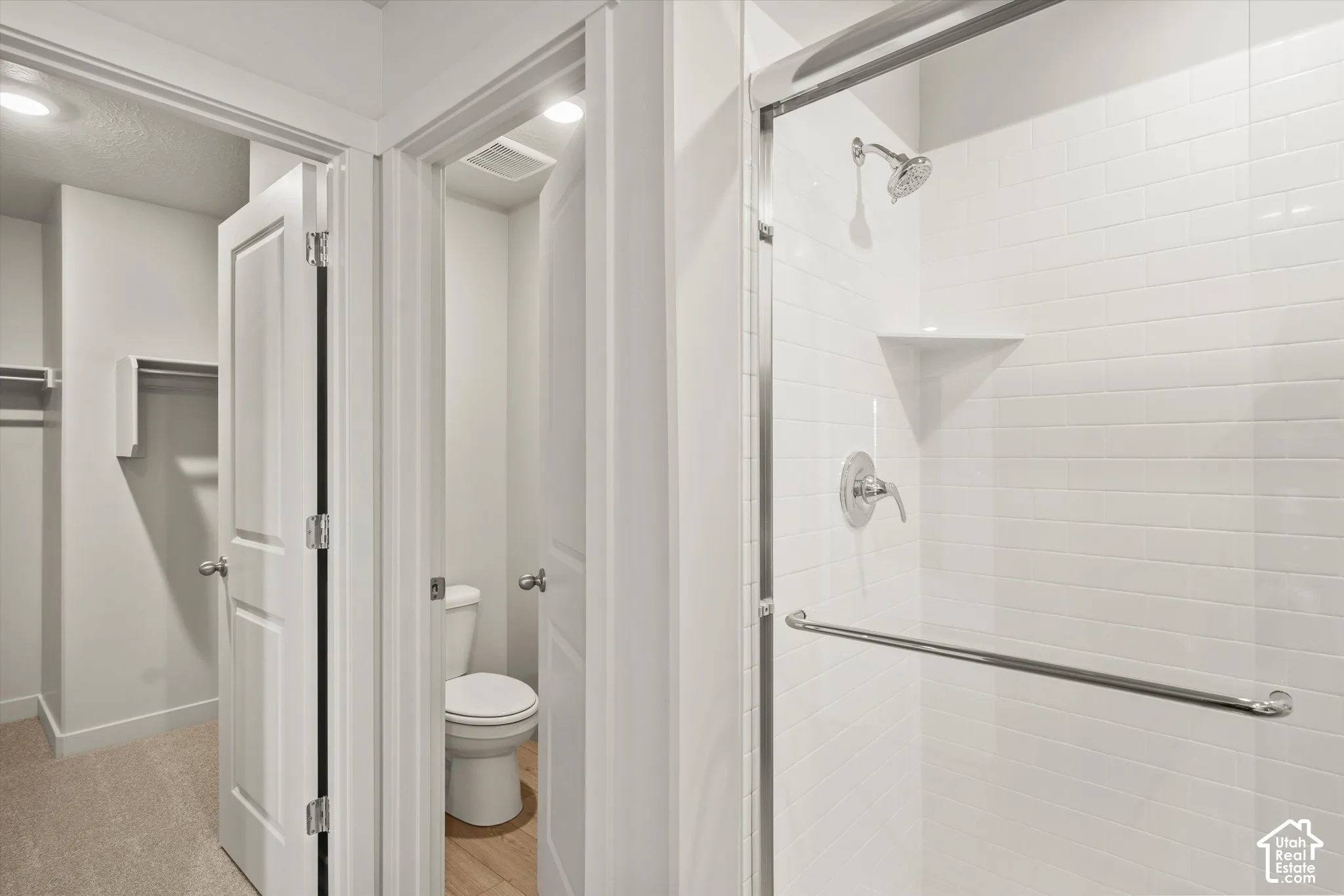 Walk-in shower featuring subway tile surround, chrome fixtures, integrated corner shelving, and a glass door with a chrome handle, complemented by a water closet and built-in closet shelving