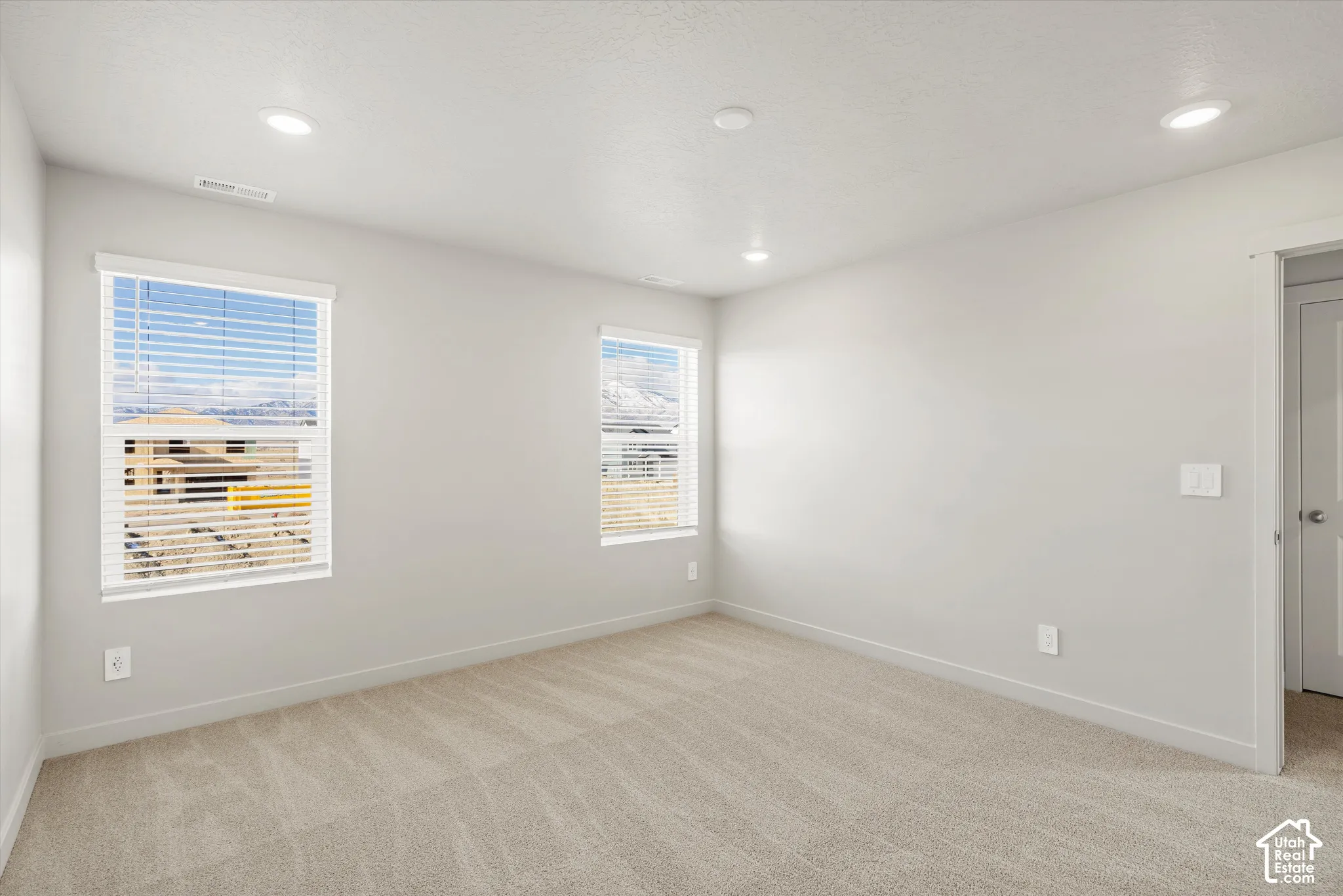 Neutral-toned room featuring textured carpeting, recessed lighting, and double windows with adjustable horizontal blinds