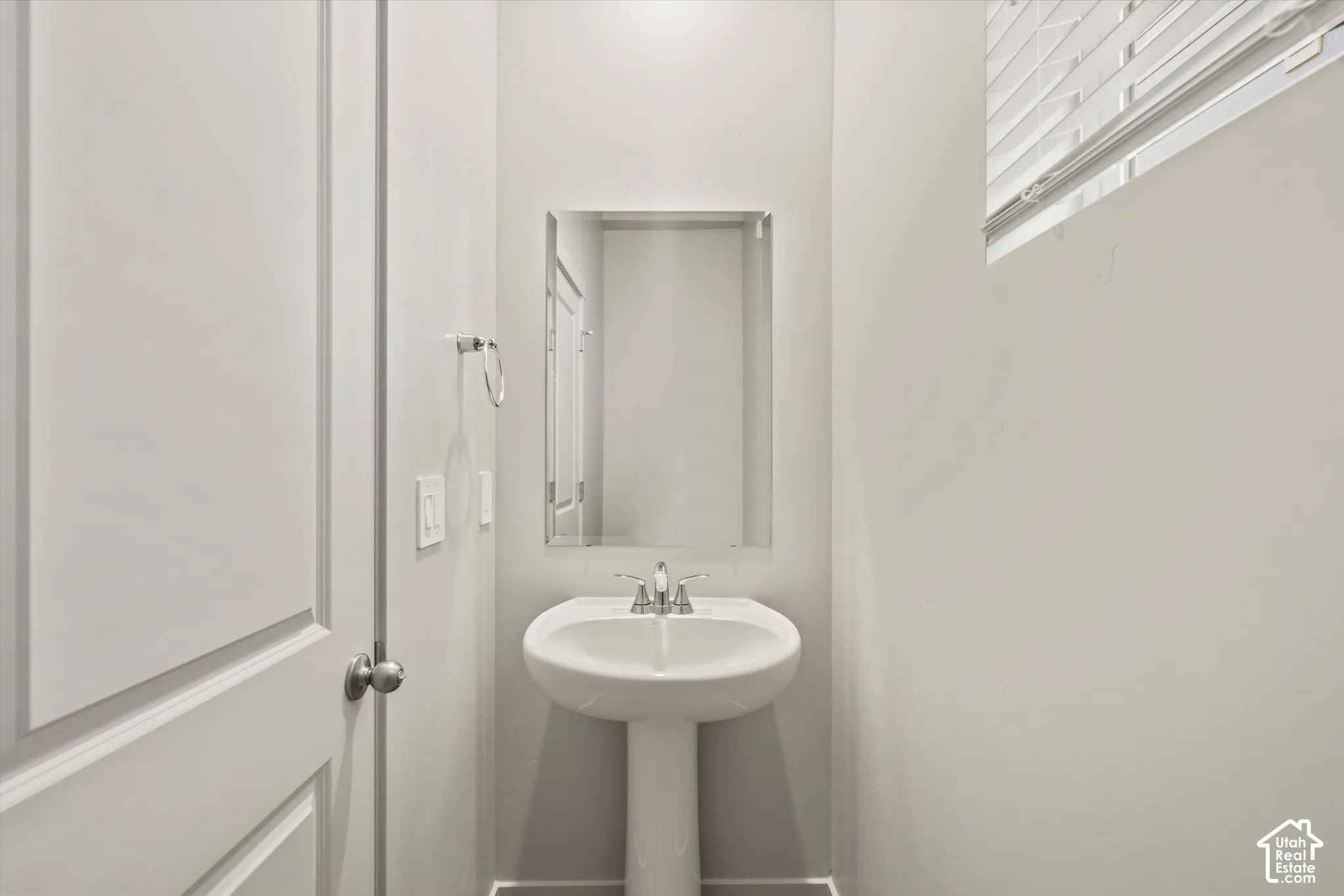 Pedestal sink with a polished chrome faucet, rectangular wall-mounted mirror, and horizontal window blinds
