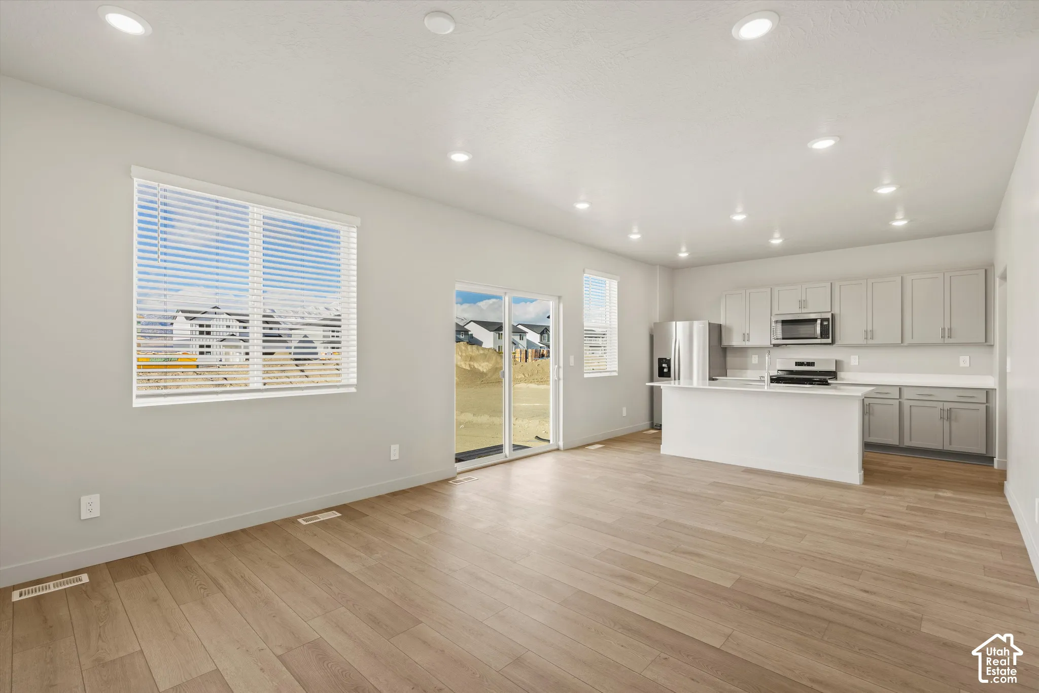 Open-concept interior featuring wood-finish flooring, recessed lighting, cabinetry with neutral-toned finish, solid-surface countertops, and glass sliding doors